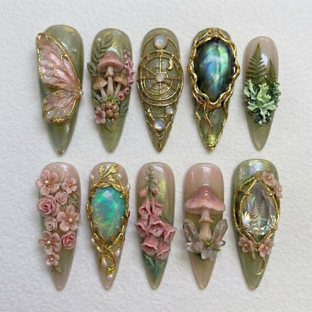 A set of ten almond-shaped press-on nails featuring intricate 3D designs including pink butterfly wings, mushrooms, gold celestial patterns, iridescent gemstones, green ferns, pink roses, foxglove flowers, and clear crystals on a sage base.