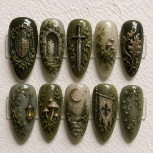 A set of ten almond-shaped press-on nails featuring intricate 3D designs in shades of forest green, cream, and metallic gold. The motifs include a shield, stone archway, sword, mushrooms, oak leaves, lantern, moon, and fleur-de-lis.