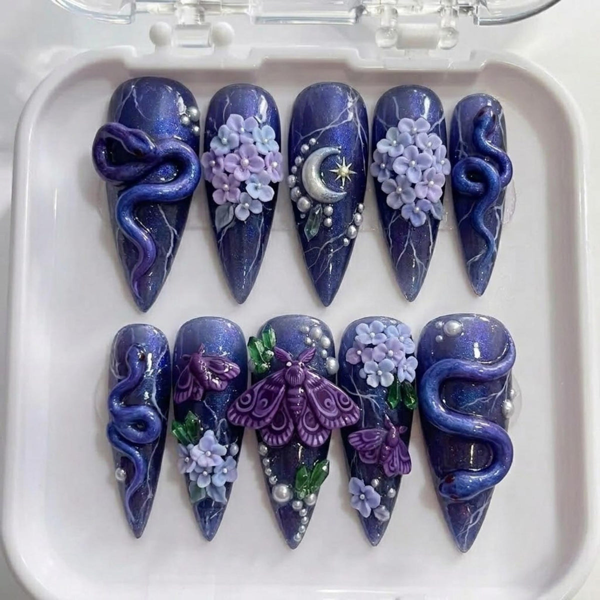 A set of ten almond-shaped press-on nails featuring a deep purple, glittery base with white lightning-like streaks. The designs include 3D purple snakes, light purple hydrangea clusters, a silver crescent moon, and purple moths.