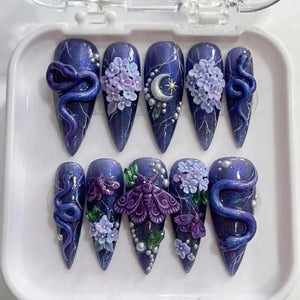 A set of ten almond-shaped press-on nails featuring a deep purple, glittery base with white lightning-like streaks. The designs include 3D purple snakes, light purple hydrangea clusters, a silver crescent moon, and purple moths.