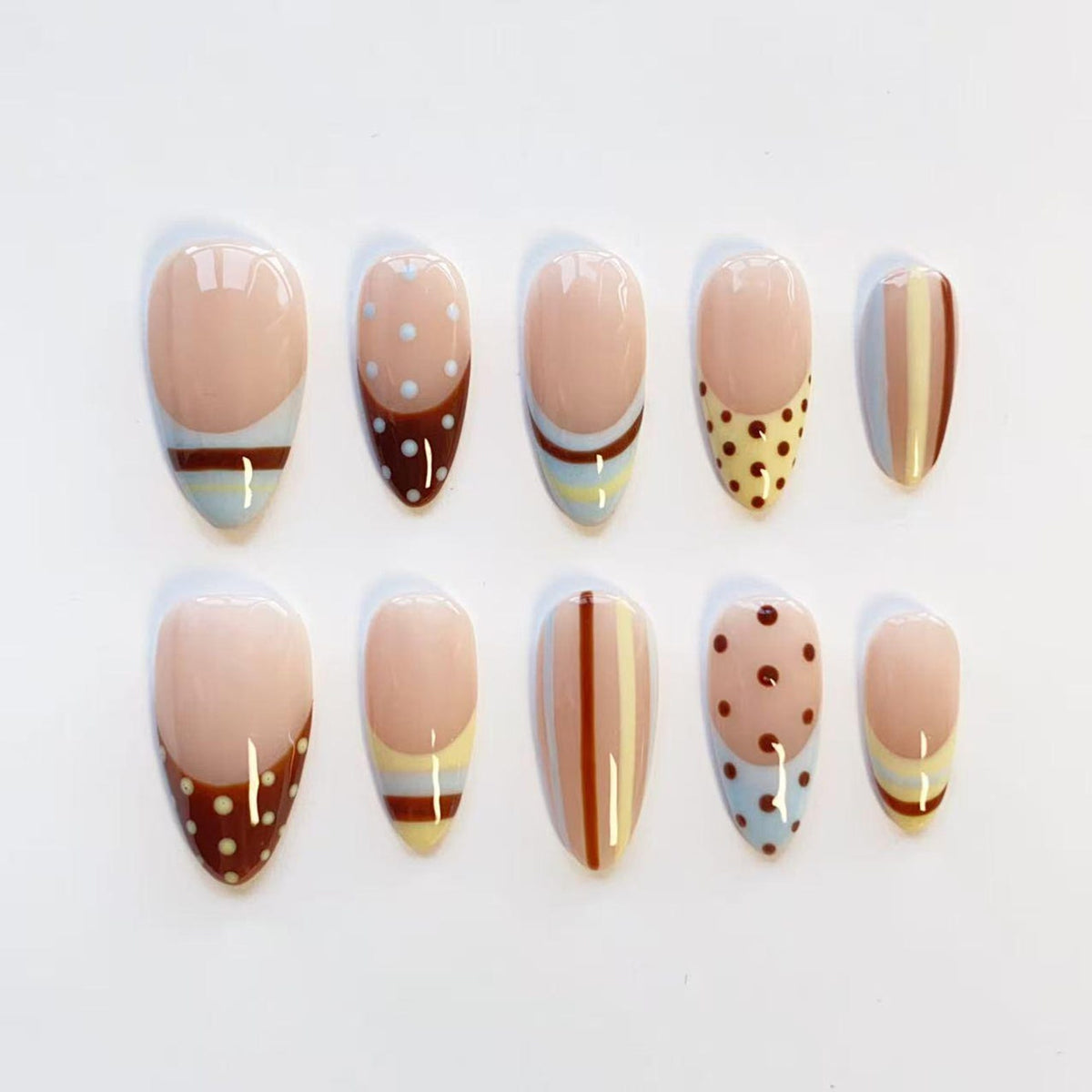 A set of ten almond-shaped press-on nails featuring a nude base with various designs including brown and light blue horizontal stripes, white polka dots on brown backgrounds, and vertical brown and cream lines on a glossy finish.