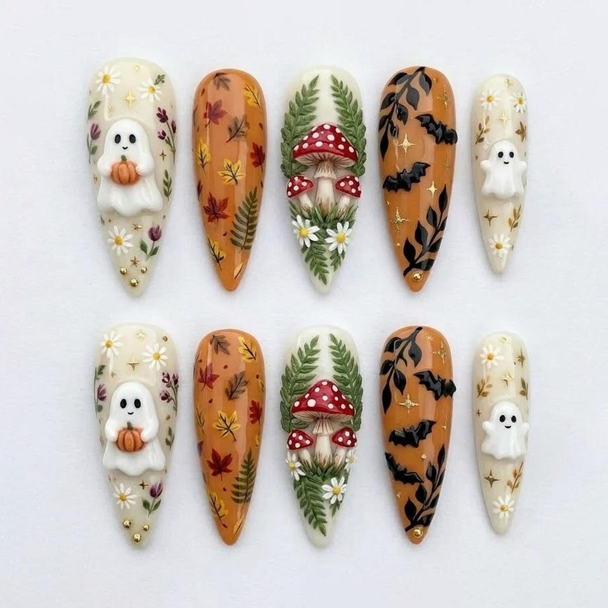 A set of ten almond-shaped press-on nails featuring autumn-themed designs. The patterns include white ghosts holding orange pumpkins, scattered fall leaves, red and white mushrooms with green ferns, black bats, and small white daisies.