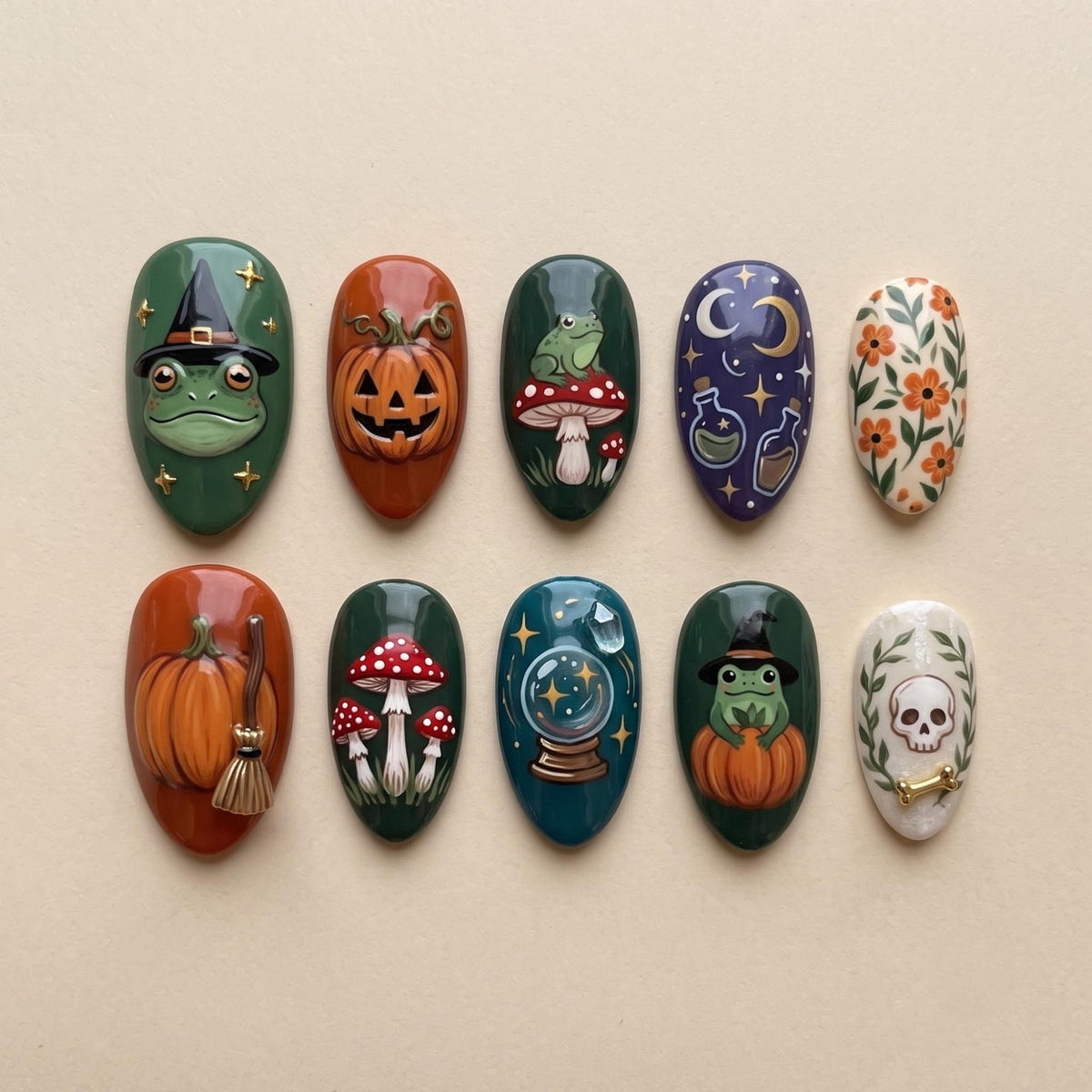 A set of ten press-on nails featuring detailed illustrations of frogs in witch hats, jack-o'-lanterns, red and white mushrooms, celestial moons, potion bottles, floral patterns, a crystal ball, and a skull with a bone accent.