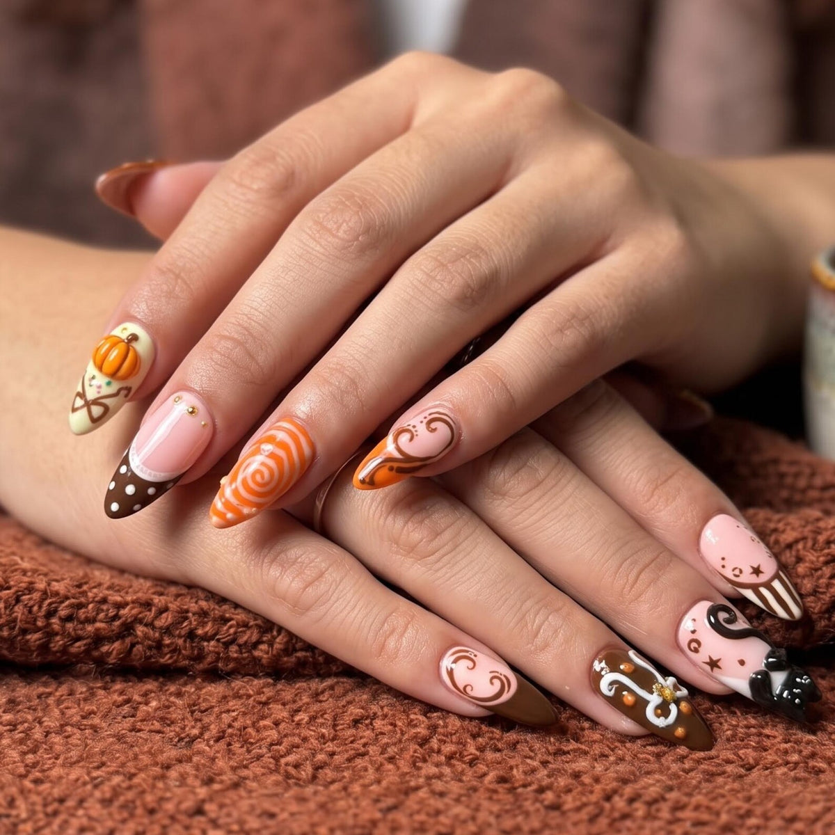 Handmade autumn press on nails with black cat, orange pumpkin, fall leaf and swirl designs in blush pink, brown, black and orange almond shapes.