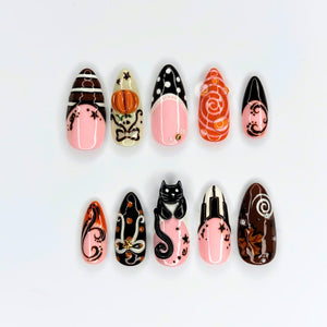 Handmade autumn press on nails with black cat, orange pumpkin, fall leaf and swirl designs in blush pink, brown, black and orange almond shapes.