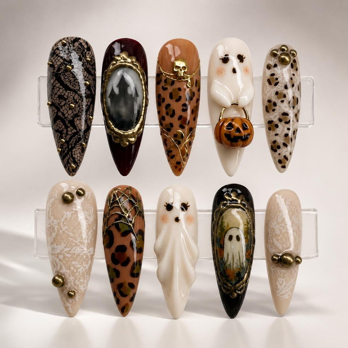 A set of ten almond-shaped press-on nails featuring Halloween-themed designs including black lace, leopard print, a 3D ghost holding a pumpkin, a skull, spider webs, and ornate framed portraits of ghosts, accented with gold studs and beads.