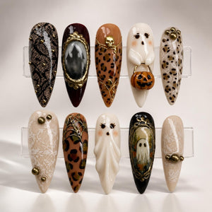 A set of ten almond-shaped press-on nails featuring Halloween-themed designs including black lace, leopard print, a 3D ghost holding a pumpkin, a skull, spider webs, and ornate framed portraits of ghosts, accented with gold studs and beads.