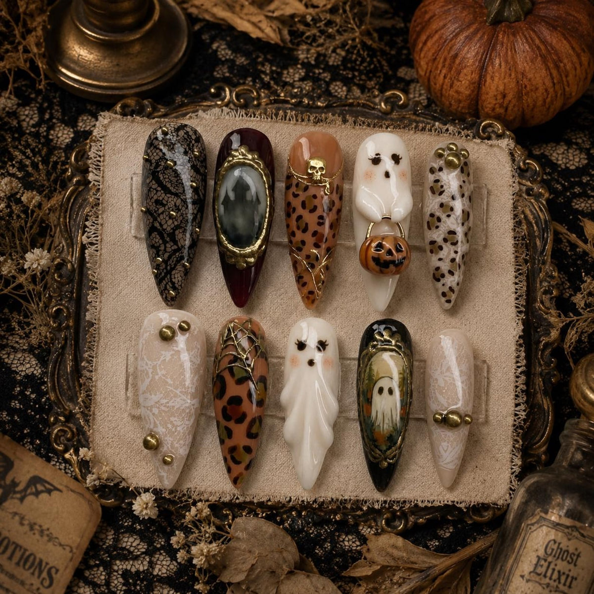 A set of ten almond-shaped press-on nails featuring Halloween-themed designs including black lace patterns, leopard print, a 3D ghost holding a pumpkin, a skull accent, a spider web, and a painted ghost inside a gold-framed oval.