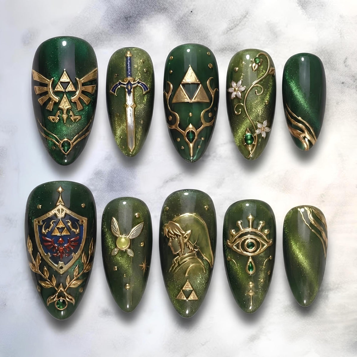 A set of ten almond-shaped press-on nails featuring a deep forest green cat-eye magnetic polish base. The designs include gold-toned emblems, a sword, a shield, a fairy, a profile silhouette, and floral accents with small gems.