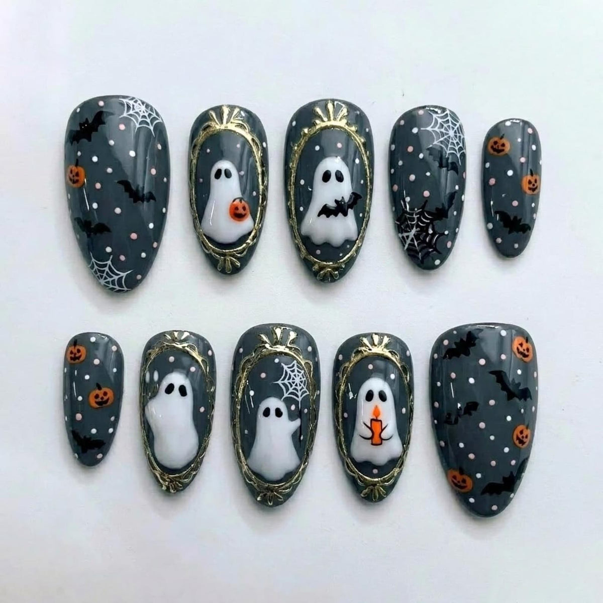 A set of ten press-on nails featuring a dark gray base with white polka dots. Designs include white ghosts, orange pumpkins, black bats, and white spiderwebs. Some nails feature gold-painted frames surrounding the ghost illustrations.
