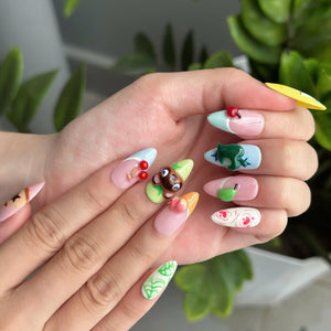 Cozy game inspired press on nails with cute animal, fruit and leaf details in pastel pink, green, blue and yellow on glossy almond shaped nails