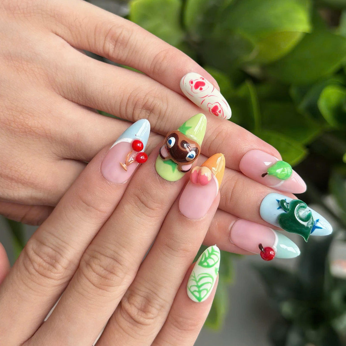 Cozy game inspired press on nails with cute animal, fruit and leaf details in pastel pink, green, blue and yellow on glossy almond shaped nails