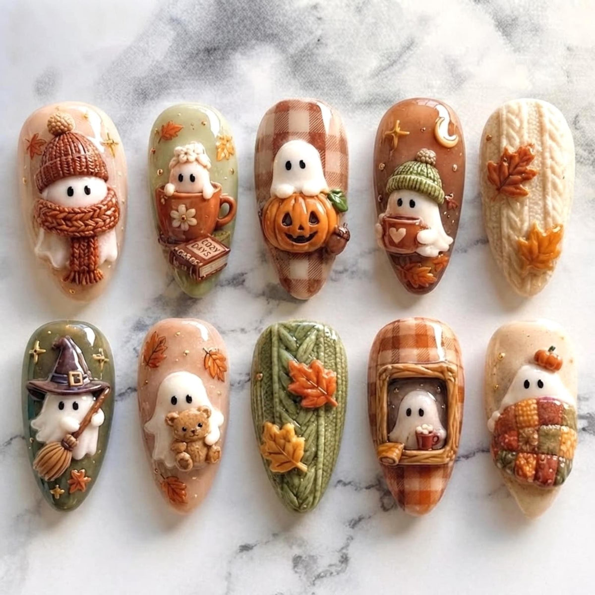 A set of ten almond-shaped press-on nails featuring 3D autumn-themed designs. The collection includes ghosts wearing knit hats and scarves, ghosts with pumpkins, a witch ghost, a ghost with a teddy bear, and textured cable knit patterns.