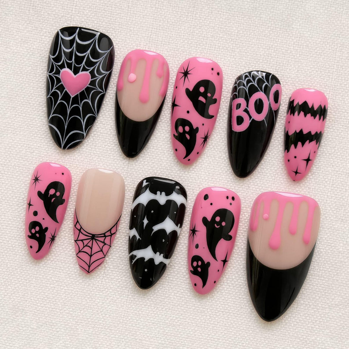 A set of ten almond-shaped press-on nails featuring a Halloween theme. Designs include black spiderwebs with a pink heart, pink slime drips on a nude base, black ghosts on pink, the word BOO in pink, black bats, and pink spiderwebs.