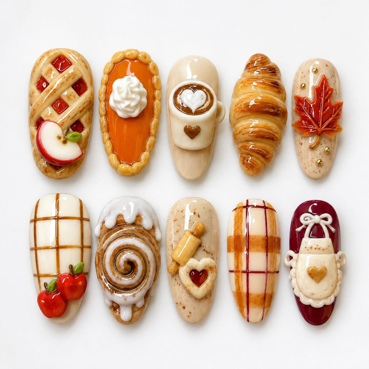 A set of ten decorative nail art pieces featuring miniature food and kitchen themes, including an apple pie, pumpkin pie, coffee mug, croissant, maple leaf, plaid pattern with apples, cinnamon roll, rolling pin, plaid, and an apron.