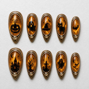 A set of ten almond-shaped press-on nails featuring a shimmering amber-orange background with black Halloween-themed silhouettes including a jack-o'-lantern, ghost, witch hat, cat, bats, haunted house, tree, and tombstone, each with a small crystal.