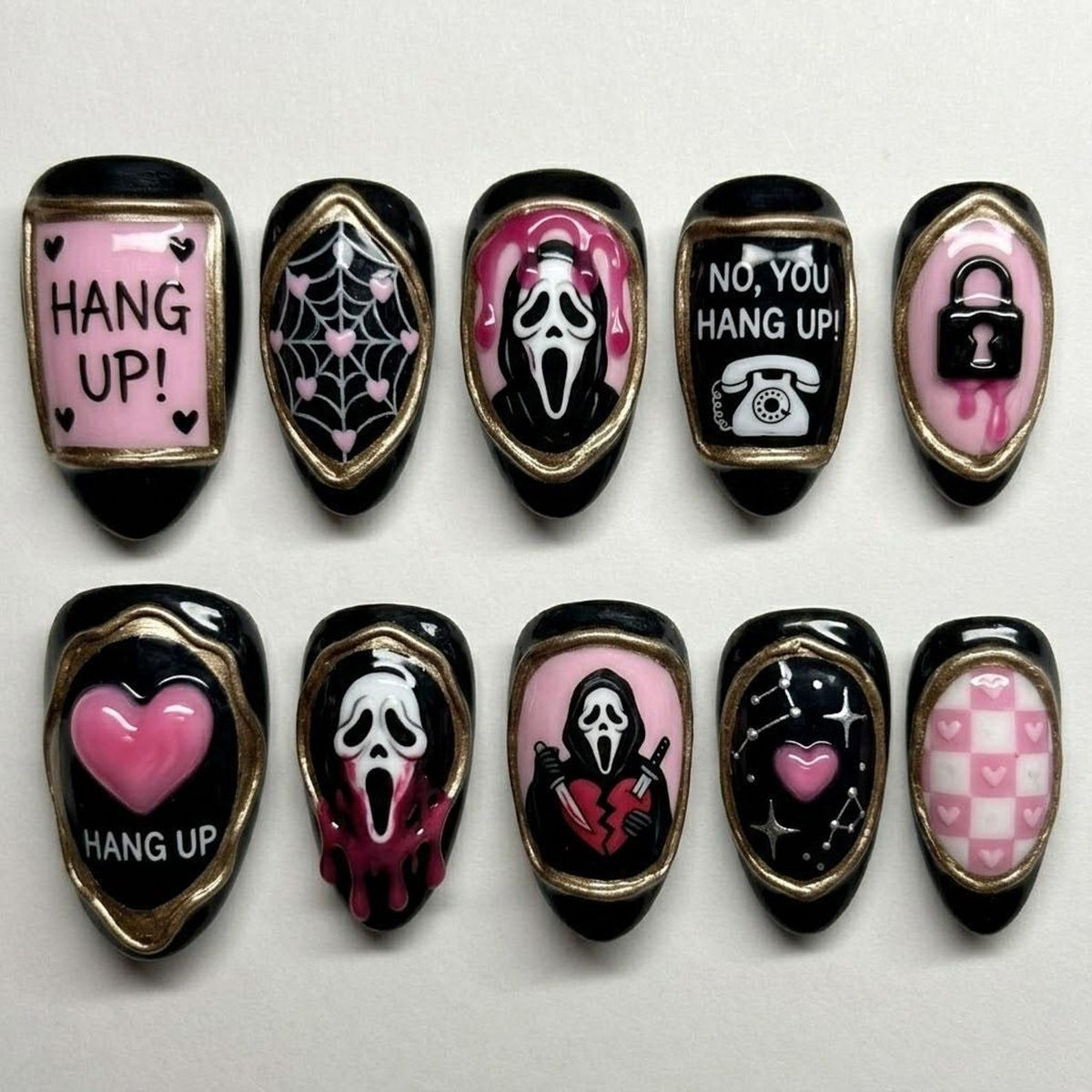 A set of ten press-on nails featuring black and pink designs with gold accents. The nails display horror-themed imagery including ghost masks, knives, hearts, spider webs, a telephone, a padlock, and text reading HANG UP! and NO, YOU HANG UP!