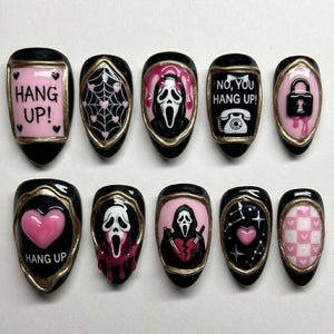 A set of ten press-on nails featuring black and pink designs with gold accents. The nails display horror-themed imagery including ghost masks, knives, hearts, spider webs, a telephone, a padlock, and text reading HANG UP! and NO, YOU HANG UP!