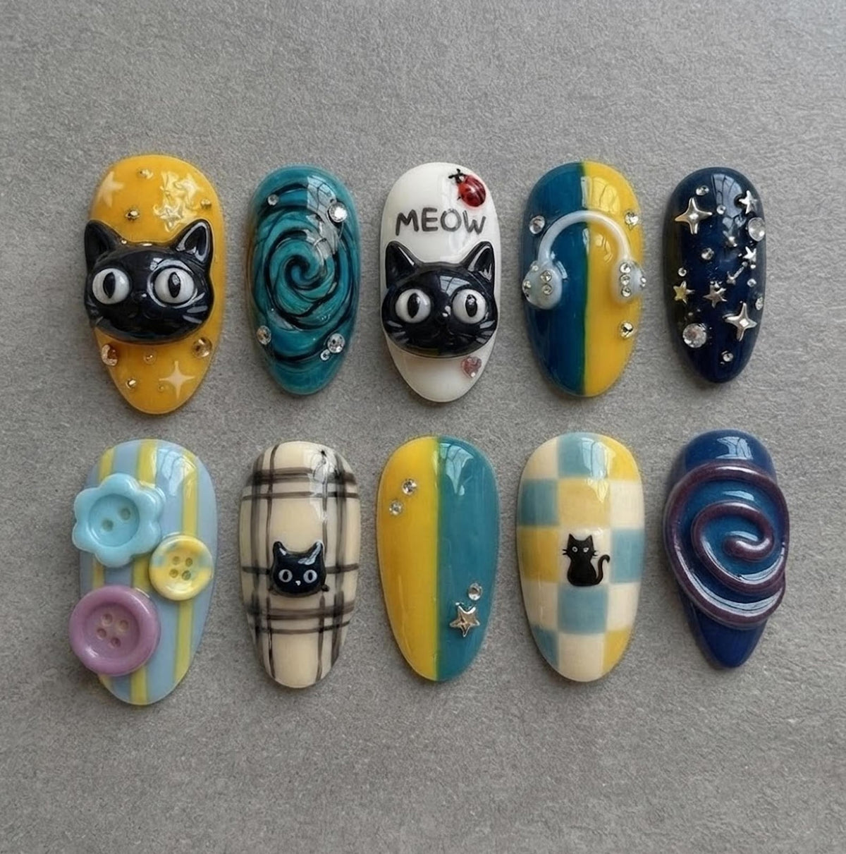 A set of ten press-on nails featuring various designs including black cat faces, blue swirls, a white nail with the text MEOW and a ladybug, headphones, stars, buttons, plaid patterns, and checkered prints with small cat silhouettes.