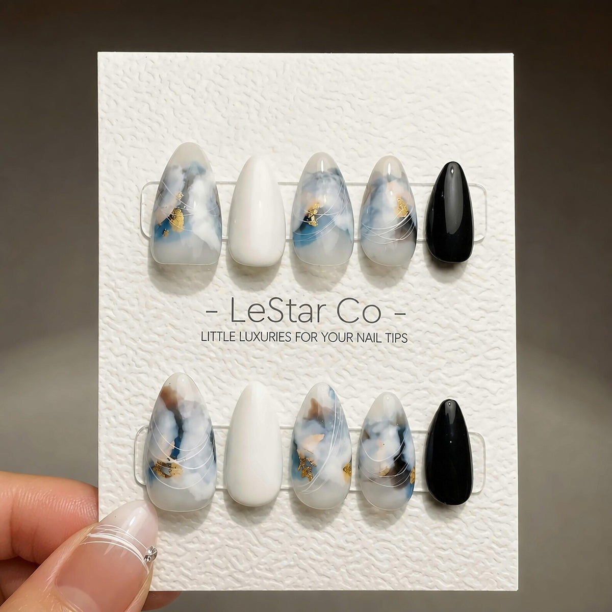 A set of ten almond-shaped press-on nails displayed on a white textured card labeled LeStar Co. The nails feature a mix of solid white, solid black, and marbled designs in blue, grey, and white with g