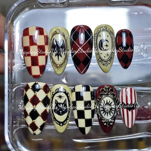 A set of ten almond-shaped press-on nails in a clear plastic case. Designs include red and cream checkerboard, black and red argyle, cream with black bat, cat, moon, and sun illustrations, and red and white stripes with a bat silhouette.