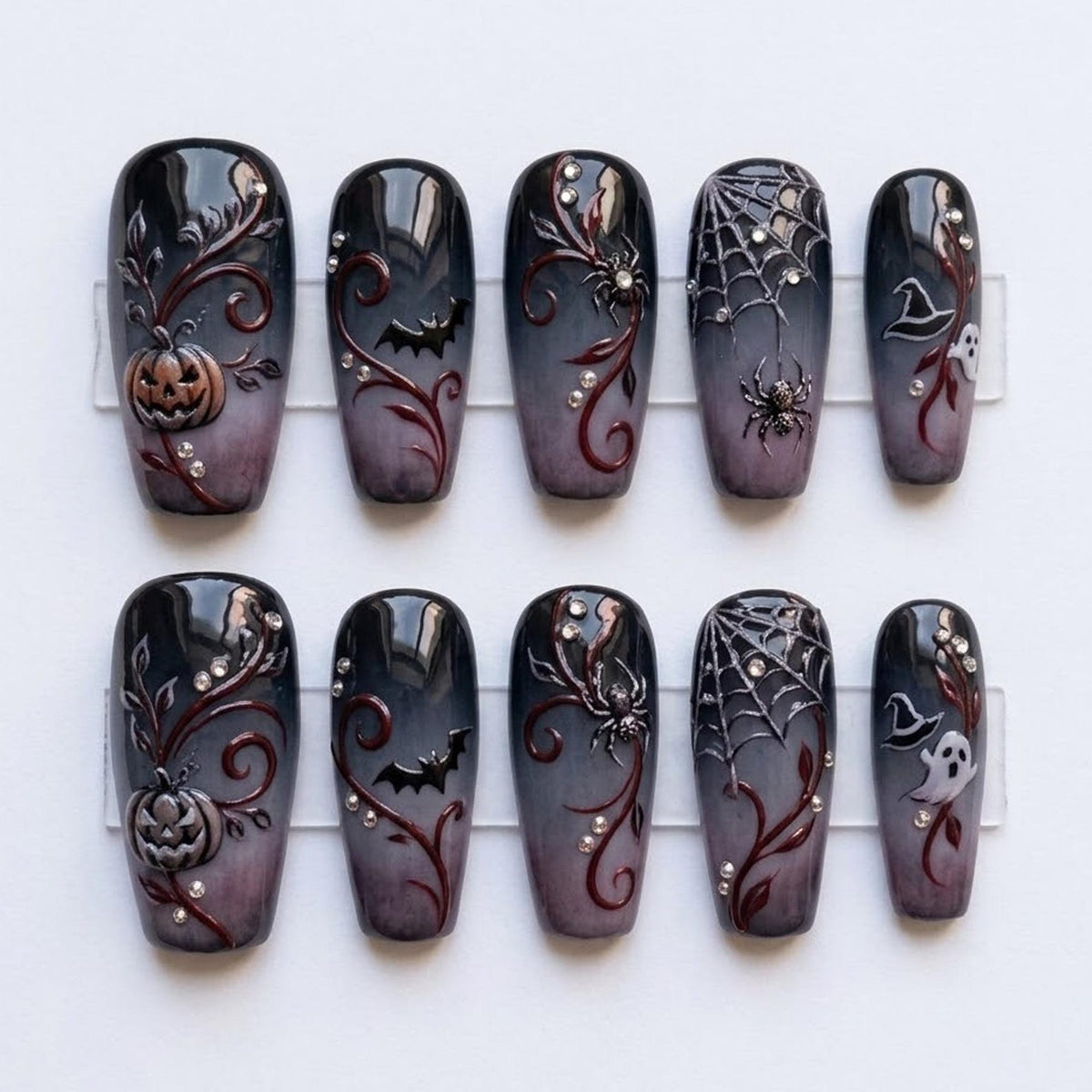 A set of ten press-on nails featuring a black to grey gradient base with raised 3D designs including pumpkins, bats, spiders, spiderwebs, witch hats, and ghosts, accented with small clear rhinestones and dark red swirling vine details.