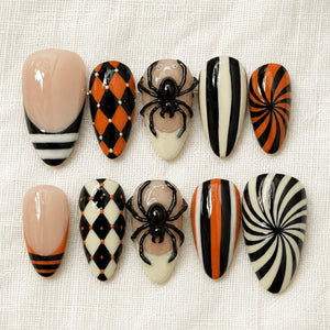 A set of ten press-on nails featuring Halloween-themed designs including black and orange harlequin patterns, a three-dimensional black spider on a nude base, vertical black and white stripes, and black and orange spiral swirls.