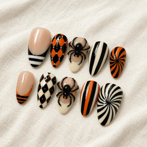 A set of ten press-on nails featuring various designs including black and orange harlequin patterns, vertical black and white stripes, orange and black swirls, and three-dimensional black spider accents on a nude base.
