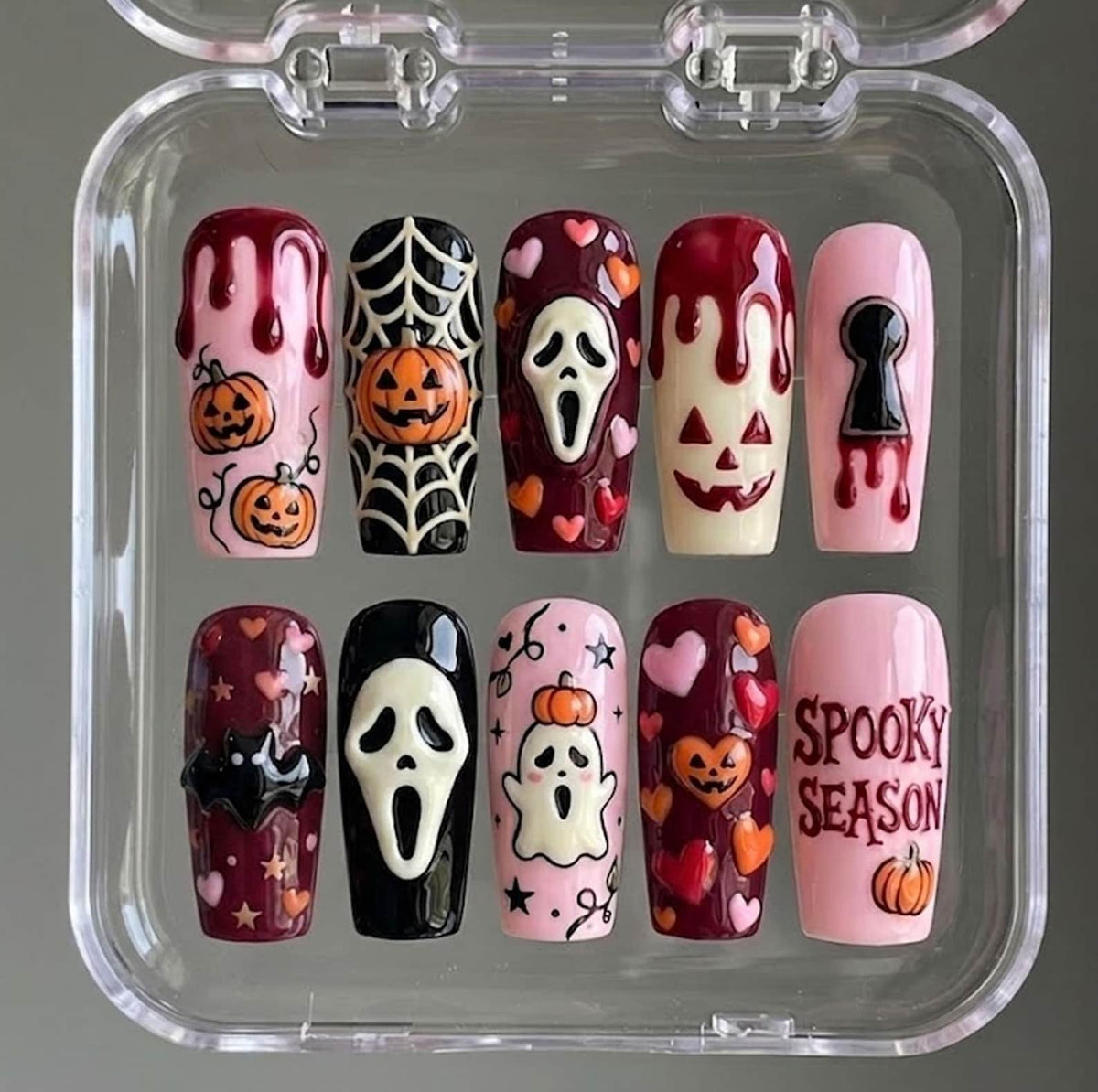 A set of ten press-on nails in a clear plastic case featuring Halloween designs including pumpkins, spider webs, a ghost, a bat, hearts, stars, a keyhole, and a screaming mask character, with the text SPOOKY SEASON on one nail.