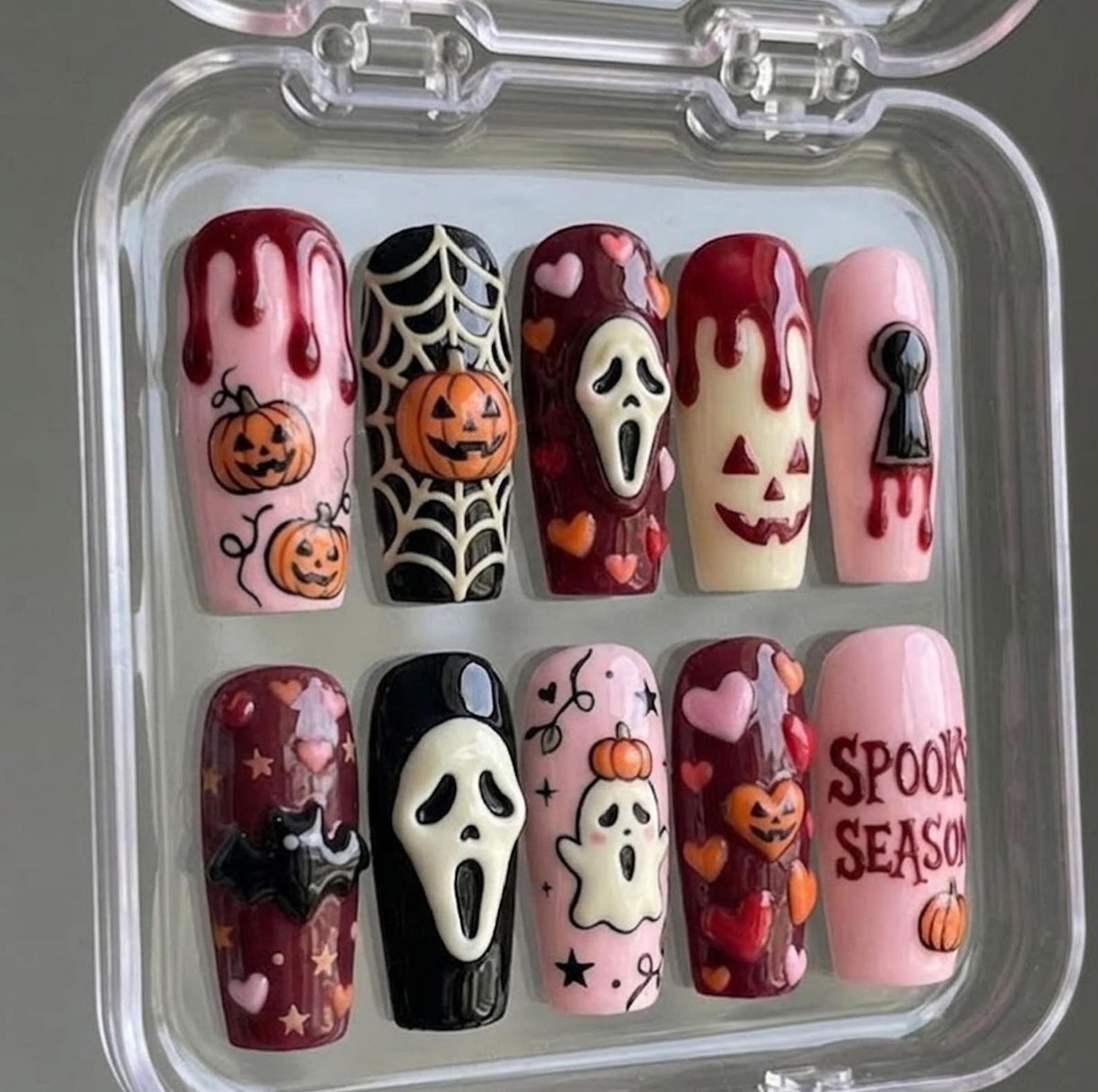 A set of ten press-on nails in a clear plastic case featuring Halloween designs. The nails include motifs of pumpkins, spider webs, ghosts, bats, hearts, a scream mask, blood drips, a keyhole, and the text SPOOKY SEASON in red.