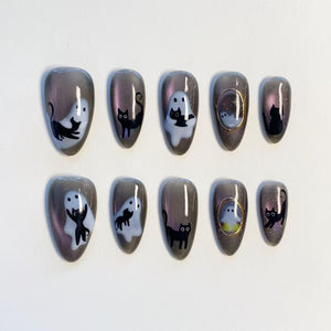A set of ten almond-shaped press-on nails featuring a dark gray magnetic shimmer base. The designs include hand-painted black cats, white ghosts, and small framed portraits, creating a cohesive Halloween-themed nail art collection.