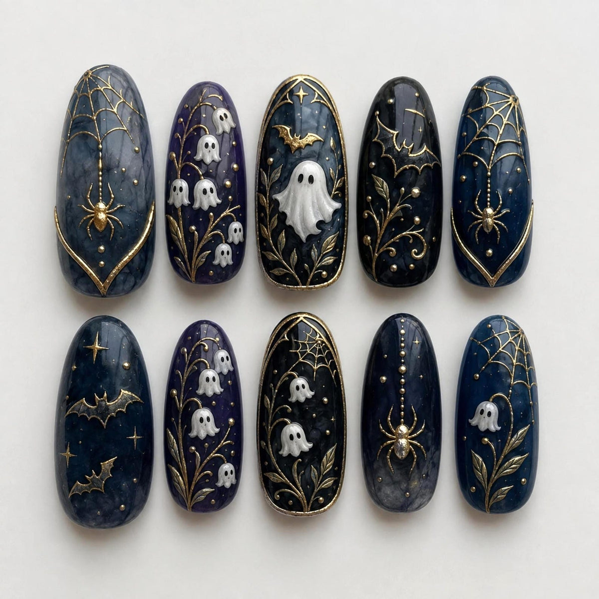 A set of ten almond-shaped press-on nails featuring dark blue and black marble backgrounds. Designs include raised white ghosts, gold metallic spider webs with spiders, lily of the valley flowers, and flying bats with gold accents.