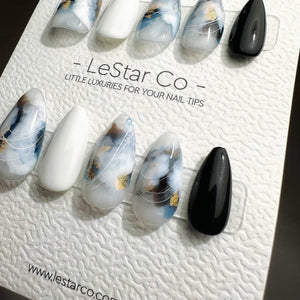 A set of ten almond-shaped press-on nails displayed on a white textured card labeled LeStar Co. Little Luxuries for Your Nail Tips. The nails feature a mix of solid white, solid black, and marbled des