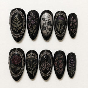 A set of ten almond-shaped press-on nails with a glossy black base. Each nail features intricate botanical or insect illustrations in silver, purple, and red tones, with some designs framed by ornate silver metallic borders.