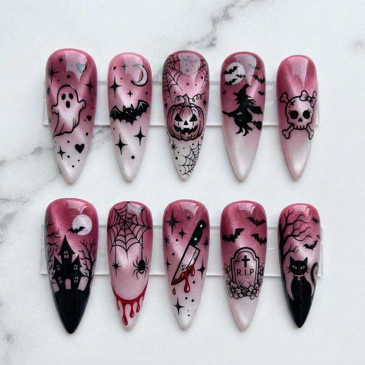 Ten almond-shaped press-on nails featuring a pink and white cat-eye gradient base with black Halloween-themed designs including a ghost, bat, pumpkin, witch, skull, haunted house, spider web, knife, tombstone with R.I.P text, and cat.