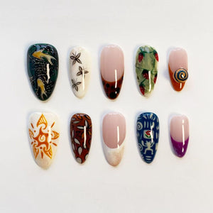 A set of ten almond-shaped press-on nails featuring diverse designs including a dark green koi fish pattern, black butterflies on white, tortoiseshell tips, strawberry prints, a blue swirl, a yellow sun, brown leaves, and a purple tip.