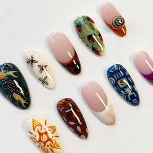 A collection of ten almond-shaped press-on nails featuring diverse designs including a strawberry pattern, a butterfly motif, a blue and white graphic print, a brown leaf pattern, a sunburst design, and several French tip variations.