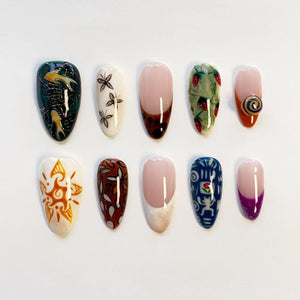 A set of ten almond-shaped press-on nails featuring diverse designs including dark green with gold koi fish, white with black butterflies, tortoiseshell French tips, strawberry patterns, a 3D spiral, sun motifs, and abstract art.