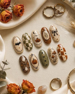 A set of ten oval-shaped press-on nails featuring various autumn and Halloween-themed designs, including ghosts, pumpkins, bats, mushrooms, bows, and checkered patterns in shades of cream, olive green, and burnt orange.