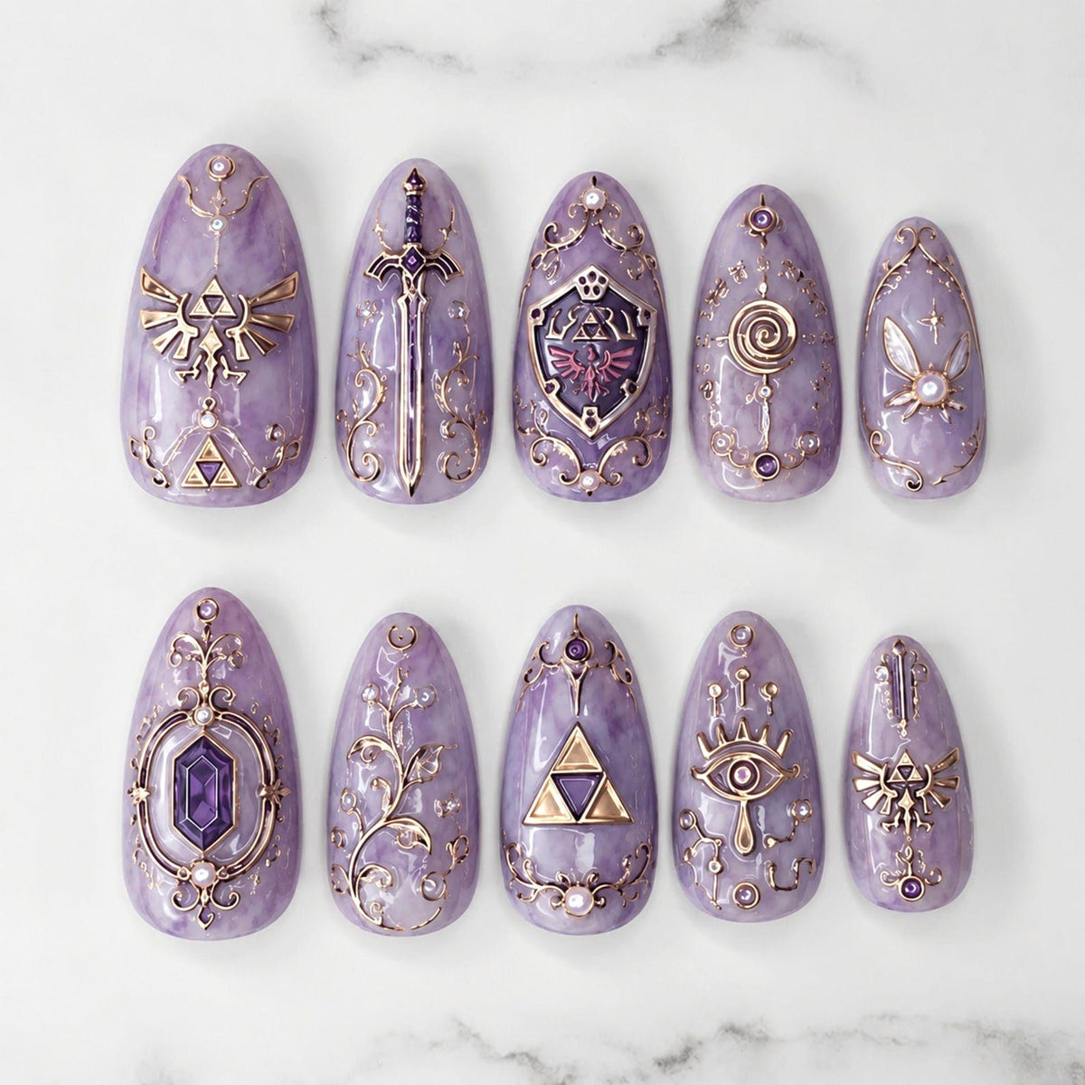 A set of ten almond-shaped press-on nails in a marbled lavender finish, featuring intricate gold-toned metallic embellishments including a sword, shield, triforce symbols, a fairy, and ornate filigree patterns with small embedded crystals.