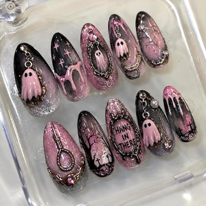 A set of ten almond-shaped press-on nails featuring a black and pink color palette with glitter, ghost charms, silver chains, and ornate frames. One nail displays the text HANG IN THERE inside a frame, while others show trees and graves.
