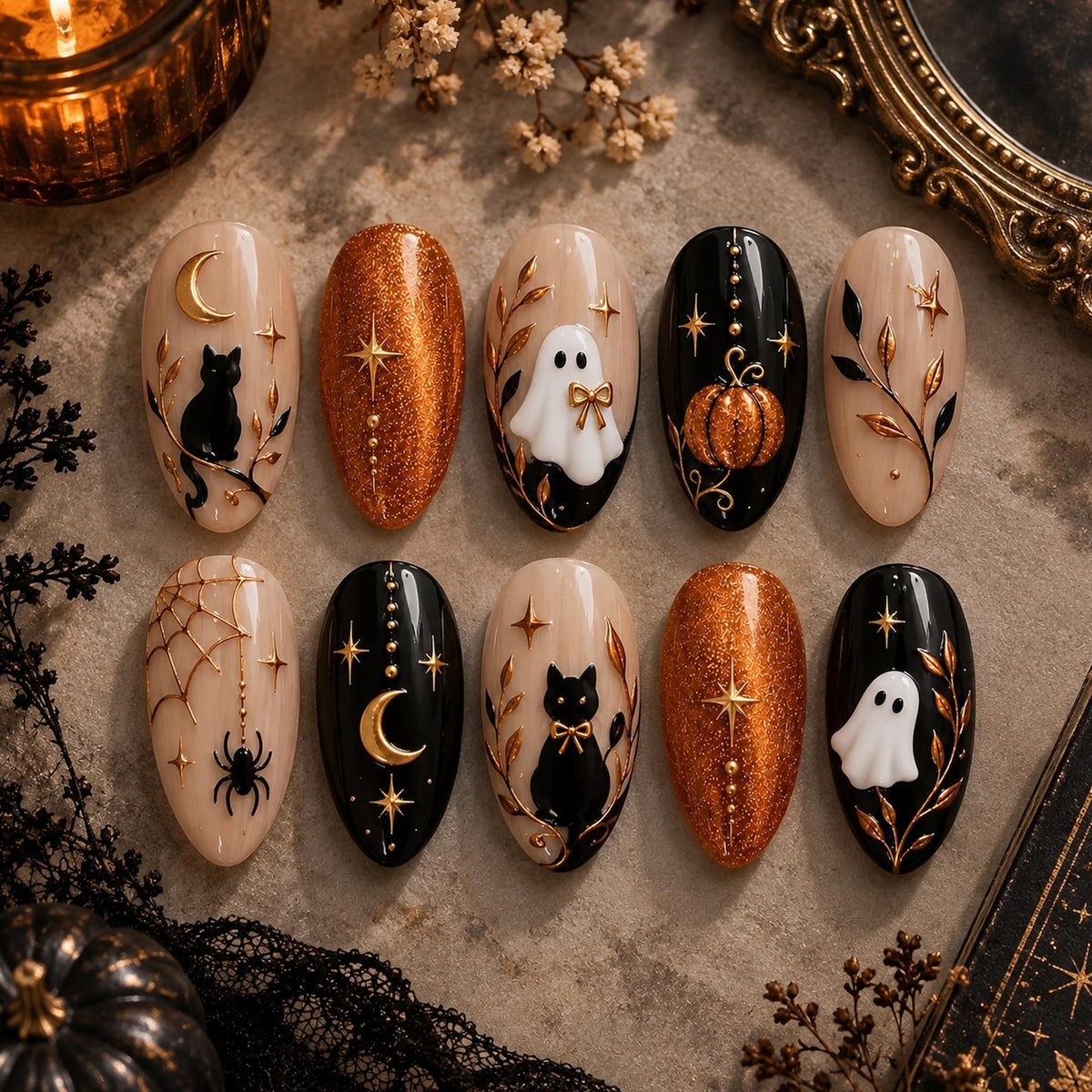 A set of ten almond-shaped press-on nails featuring Halloween designs. The nails display black cats, white ghosts, orange glitter, gold moons, stars, spiders, webs, and pumpkins on black and nude backgrounds with raised gold accents.