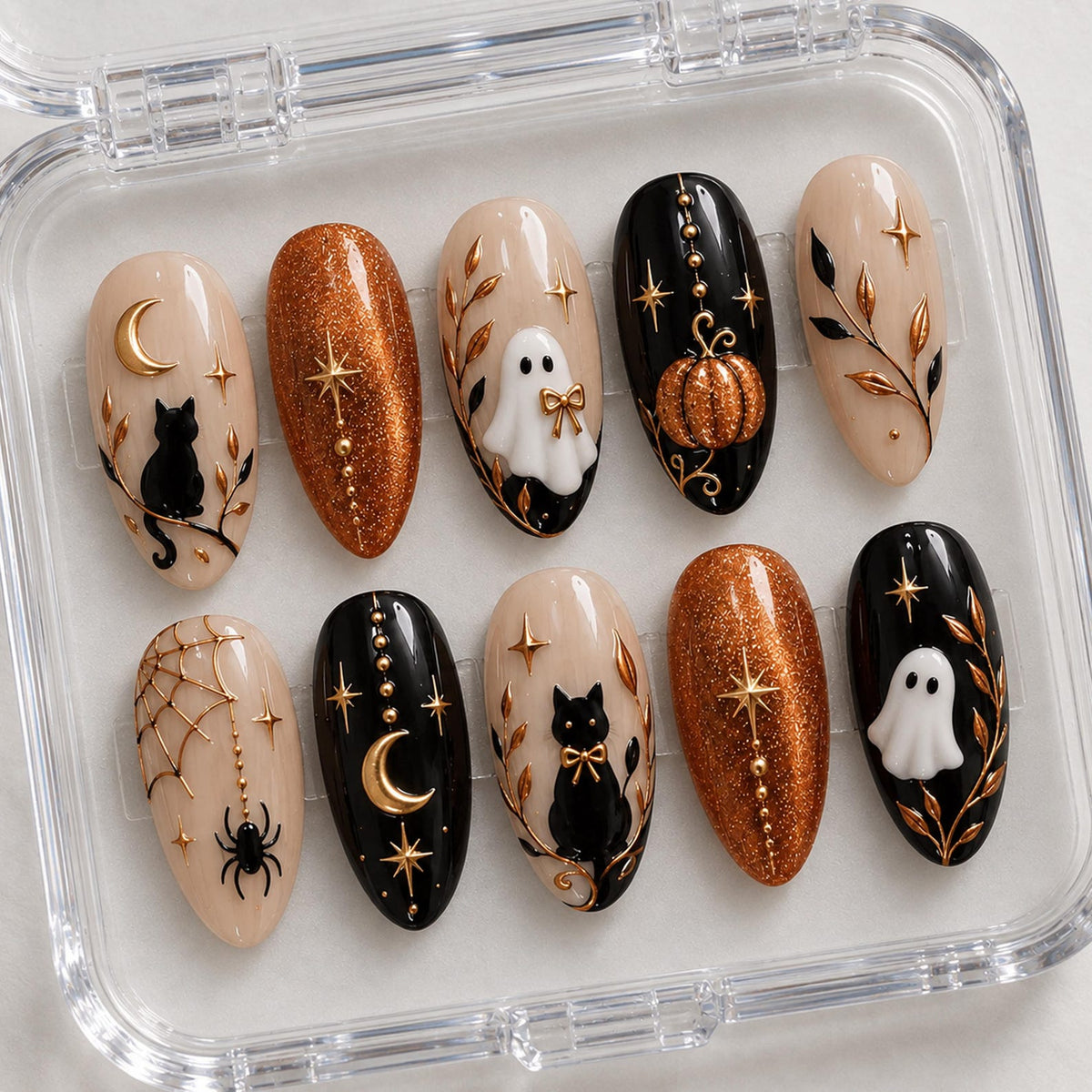 A set of ten almond-shaped press-on nails in a clear plastic case. The designs feature black cats, white ghosts, orange glitter, gold stars, moons, pumpkins, spiders, and webs on black and nude backgrounds with raised gold accents.