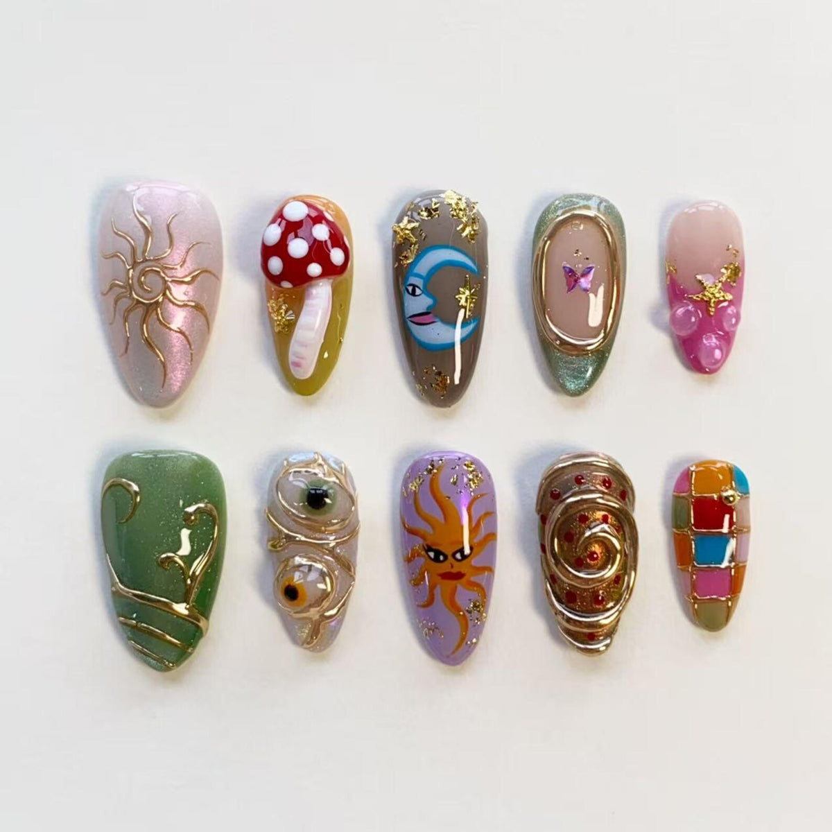 A set of ten almond-shaped press-on nails featuring diverse designs including a gold sun, a red mushroom, a blue crescent moon, a butterfly, pink accents, green swirls, realistic eyes, a sun face, gold spirals, and a colorful checkered pattern.