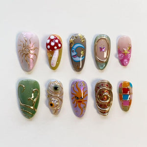 A set of ten almond-shaped press-on nails featuring diverse designs including a gold sun, a red mushroom, a blue crescent moon, a butterfly, pink accents, green swirls, realistic eyes, a sun face, gold spirals, and a colorful checkered pattern.
