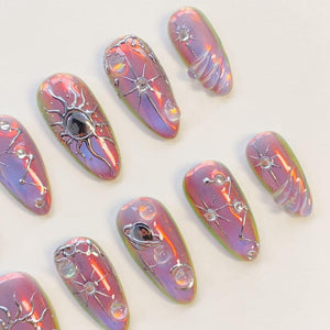 A set of ten almond-shaped press-on nails featuring an iridescent purple and pink finish. Each nail is decorated with raised silver metallic celestial motifs, including stars, planets, and constellations, accented with small clear rhinestones.