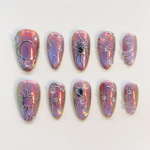 A set of ten press-on nails with an iridescent purple and pink finish. Each nail features raised silver celestial designs including suns, moons, stars, and planets, accented with small clear spherical beads and embedded rhinestones.