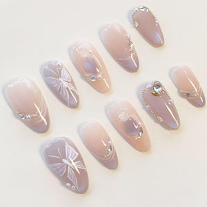 A set of ten almond-shaped press-on nails featuring a soft nude and lavender gradient base. The design includes hand-painted white butterfly wings, small iridescent rhinestones, and tiny white pearls arranged in delicate patterns.