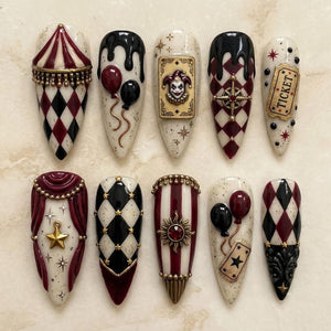 A set of ten almond-shaped press-on nails featuring a circus theme with a color palette of cream, burgundy, and black. Designs include harlequin patterns, a jester card, balloons, a ticket, a sun charm, and gold star accents.