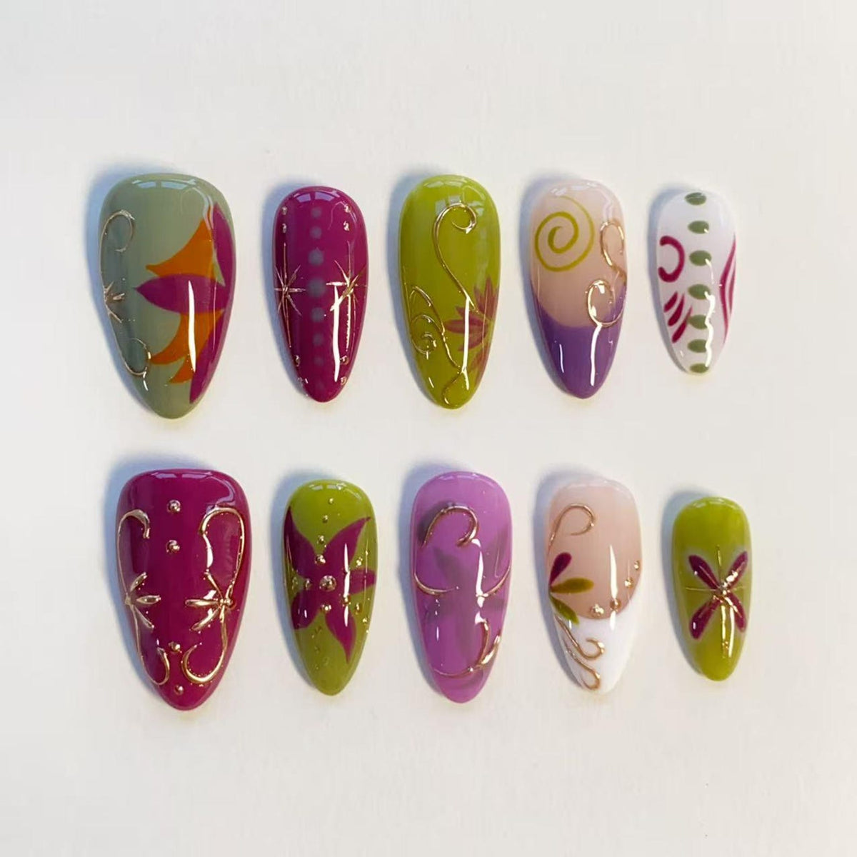 A set of ten almond-shaped press-on nails featuring a variety of designs in shades of olive green, magenta, purple, and white. The nails are decorated with intricate gold metallic line work, floral patterns, and small dots.